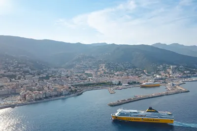 Fähre von Corsica Ferries bei der Einfahrt in den Hafen von Bastia, im Hintergrund die Stadt und das Bergland