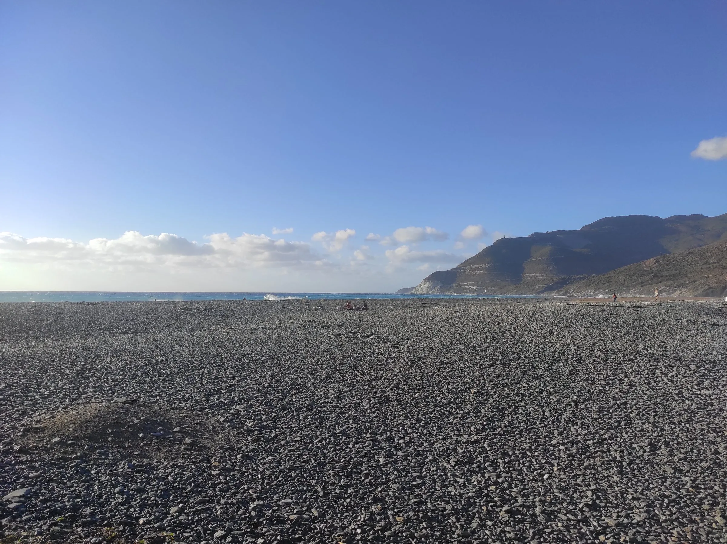 Der graugrüne Steinstrand von Nonza am Cap Corse, im Hintergrund die Steilküste